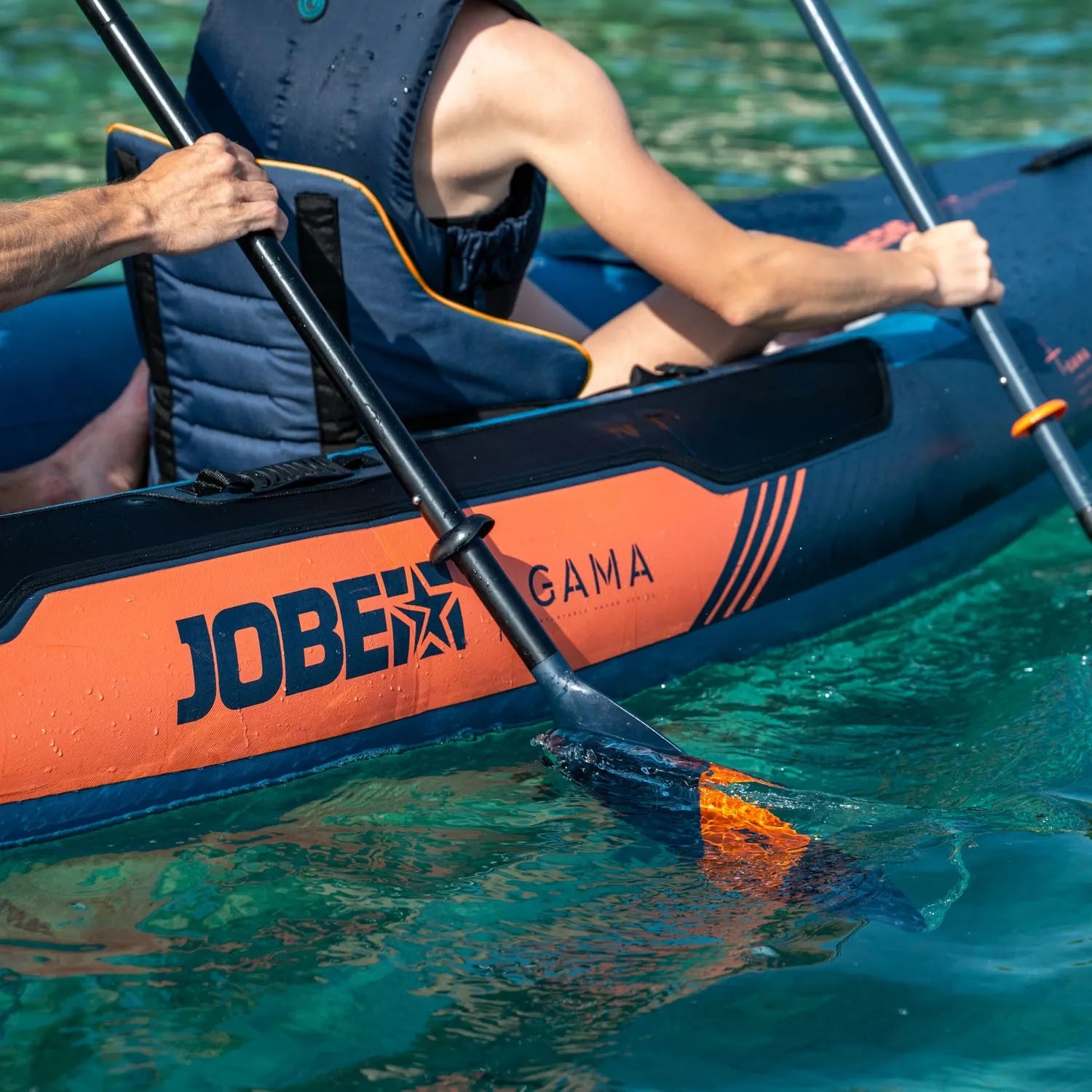 Person paddling an inflatable kayak with JOBE branding in clear blue water