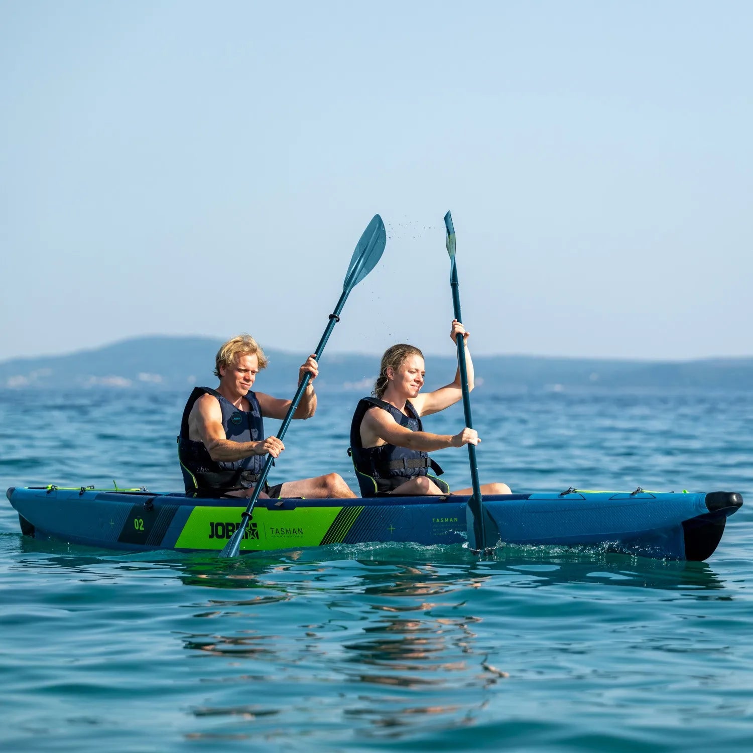 Two people paddling a kayak on calm water with a clear sky